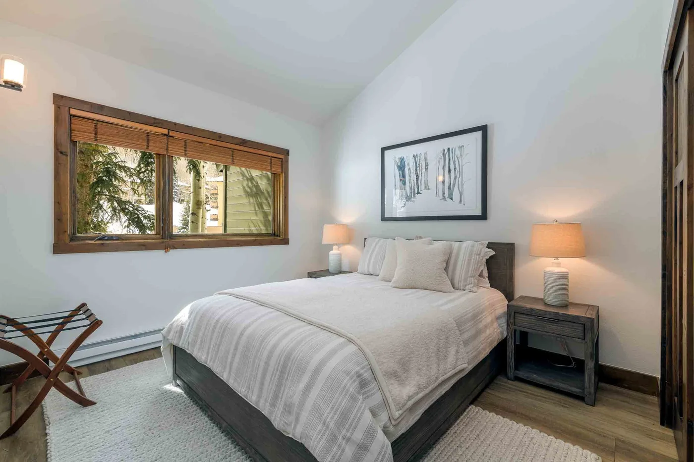 A bedroom with a neatly made bed, bedside tables, and a wide window.