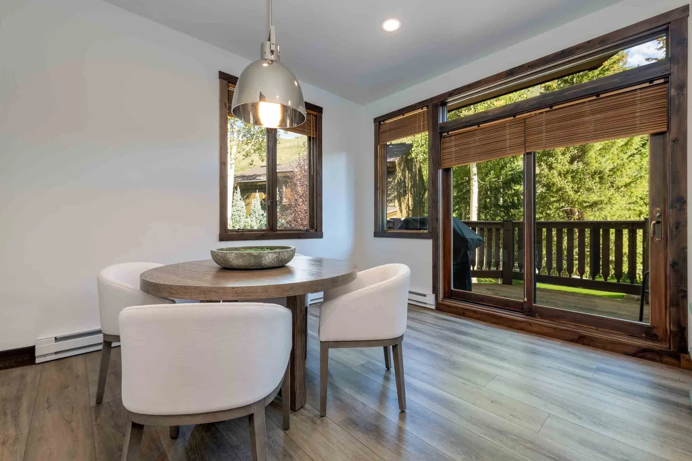 A dining area with a round table and large windows overlooking greenery.