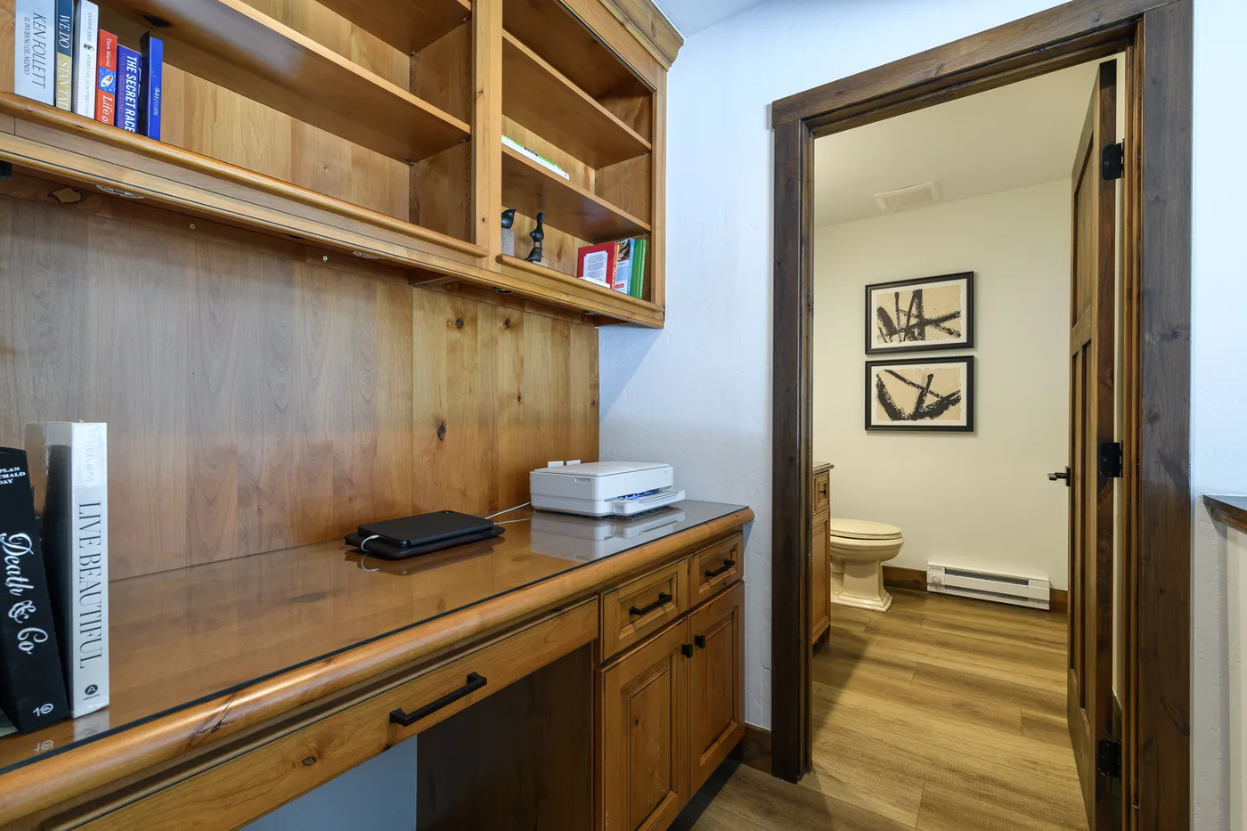 A wooden desk with open shelving sits beside a doorway to a bathroom.