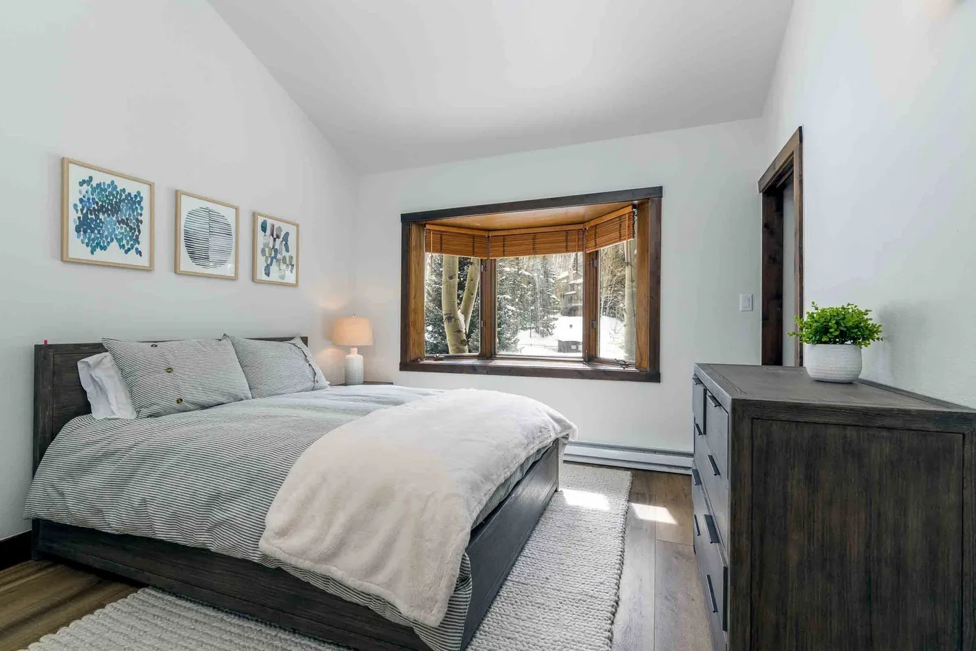 A bedroom with a bed beneath framed artwork and a large window.