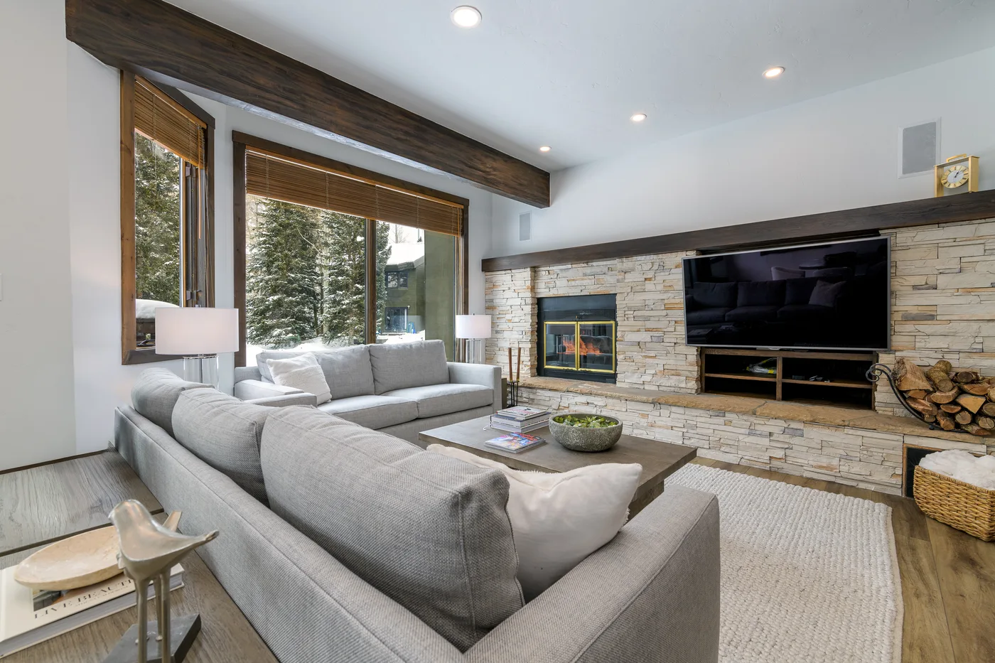 A bright living room with seating facing a television and stone fireplace.