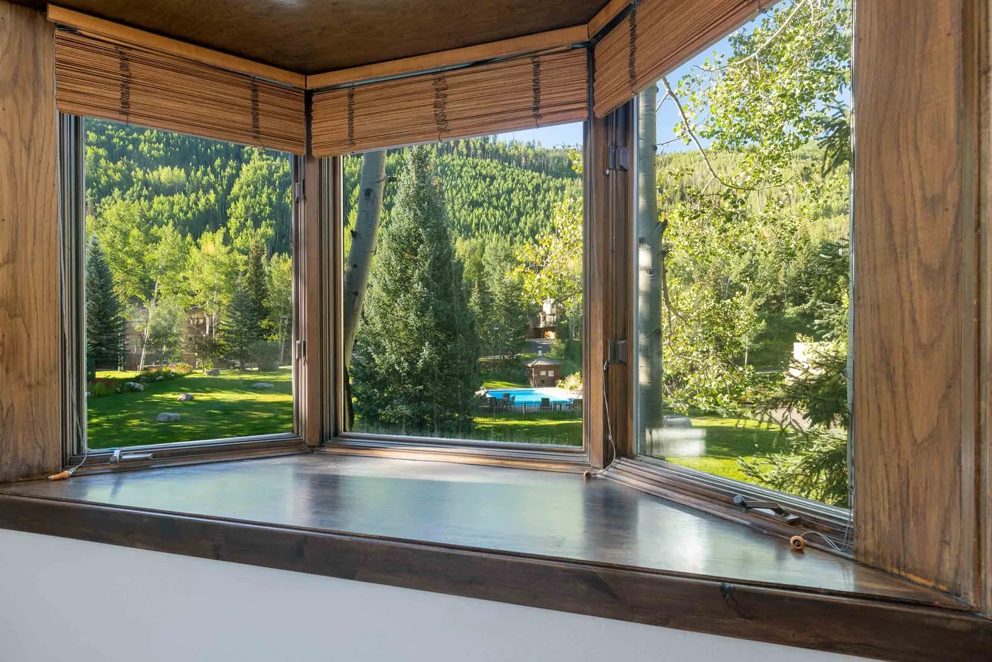 A windowed room overlooks a green garden with trees and a small pool.