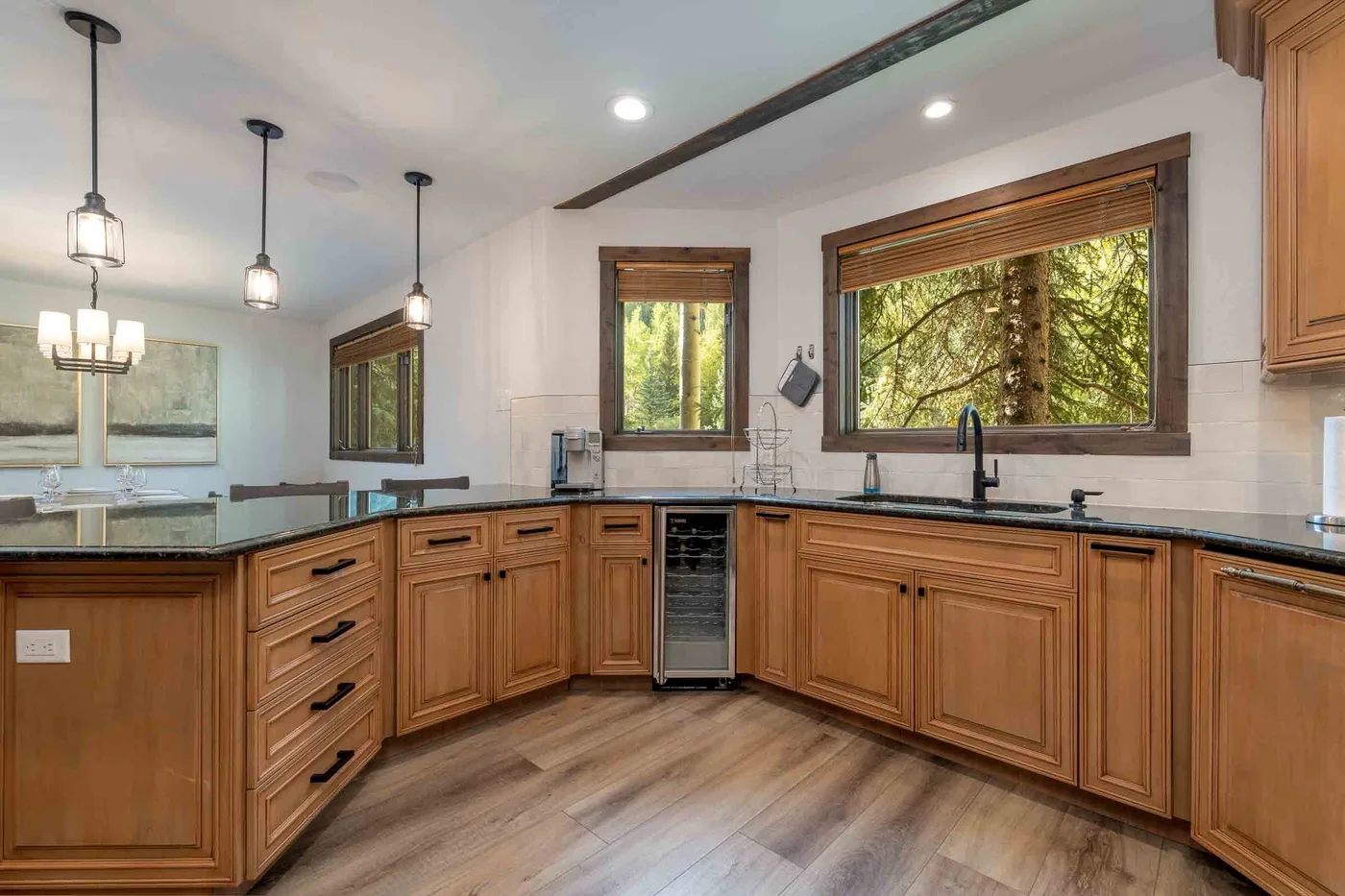 A kitchen with wooden cabinets, dark countertops, and windows overlooking trees.