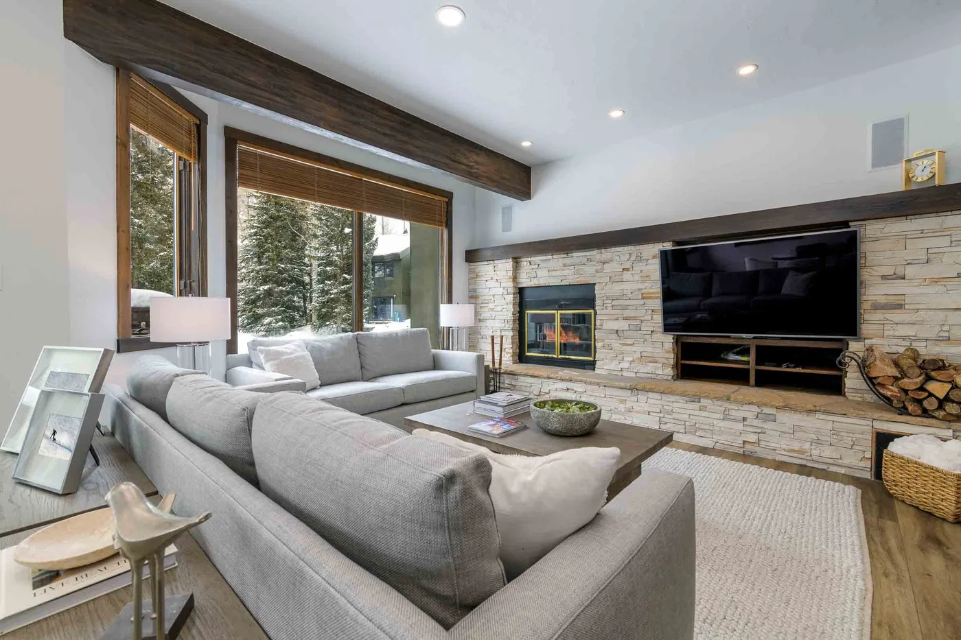 A living room with sectional seating facing a stone fireplace and television.