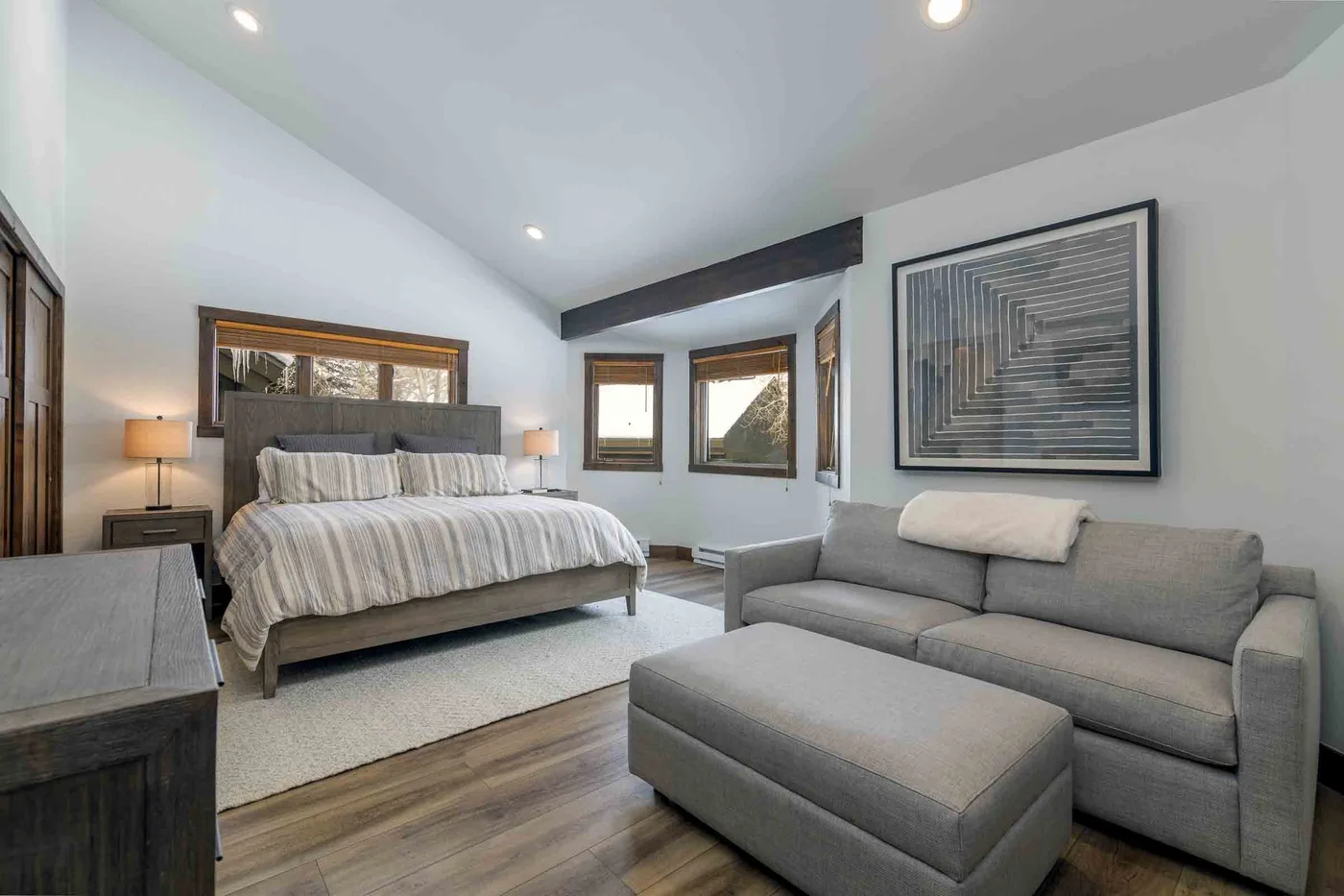 A bedroom with a bed and gray seating beneath framed wall art.