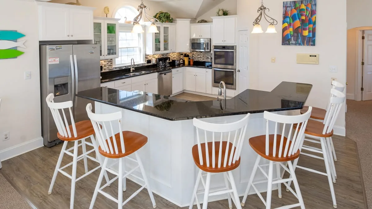 Una cocina luminosa con gabinetes blancos y una isla grande rodeada de asientos.