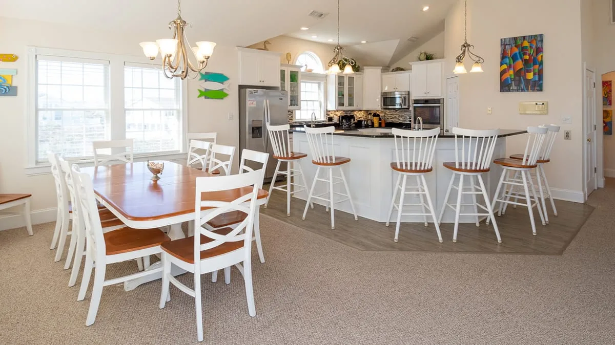 Un comedor luminoso de planta abierta con cocina, mesa de madera y barra para desayunar.