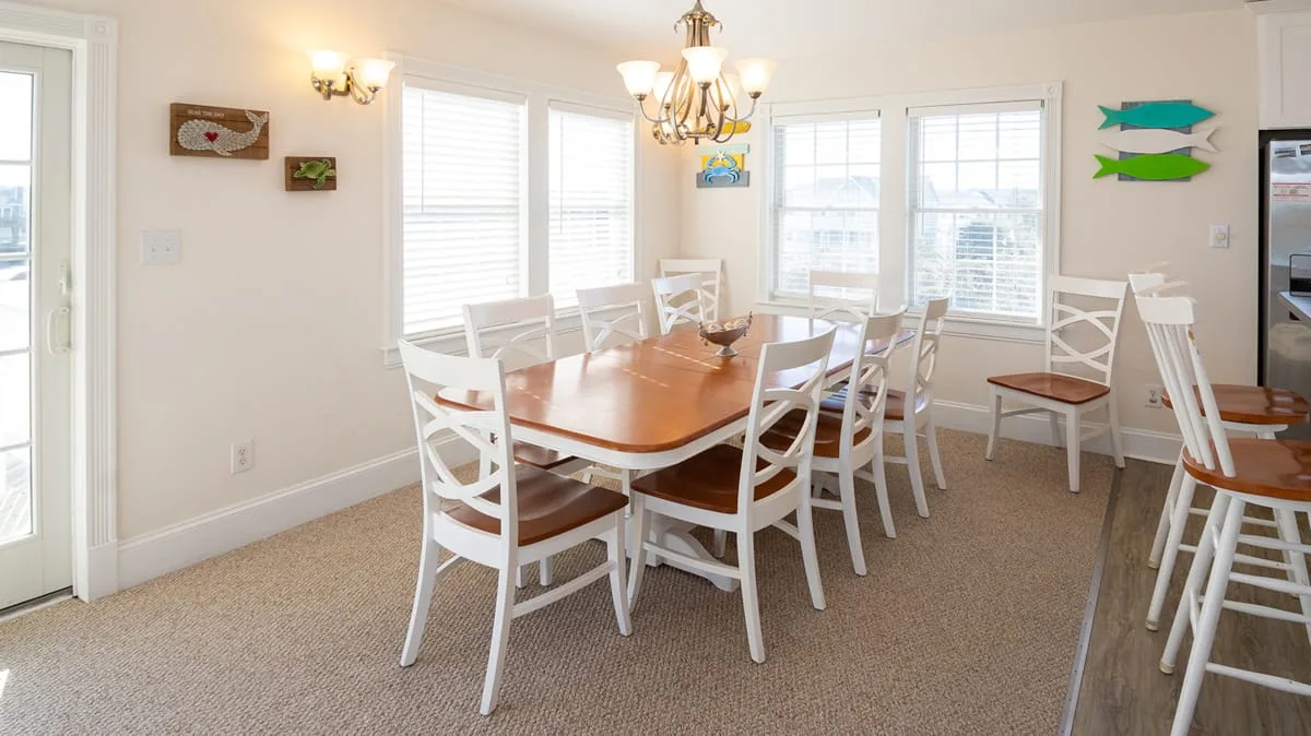Un comedor luminoso con una mesa de madera, asientos blancos y varias ventanas.