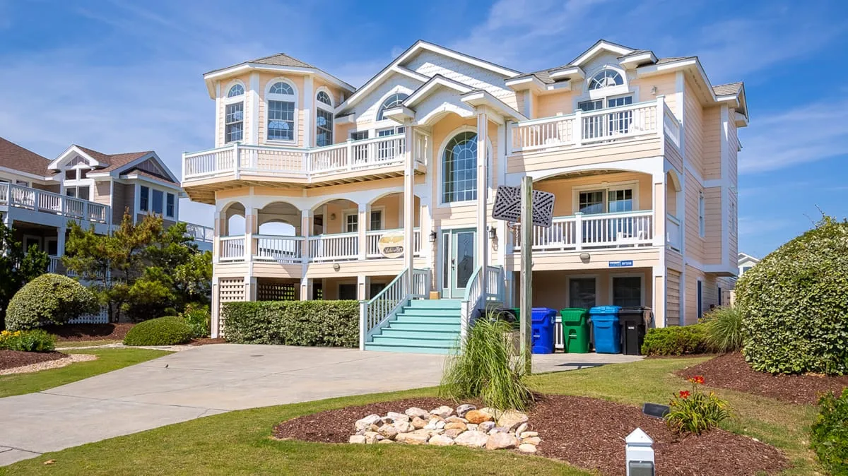 Una casa grande de estilo costero con balcones blancos y una escalera turquesa.