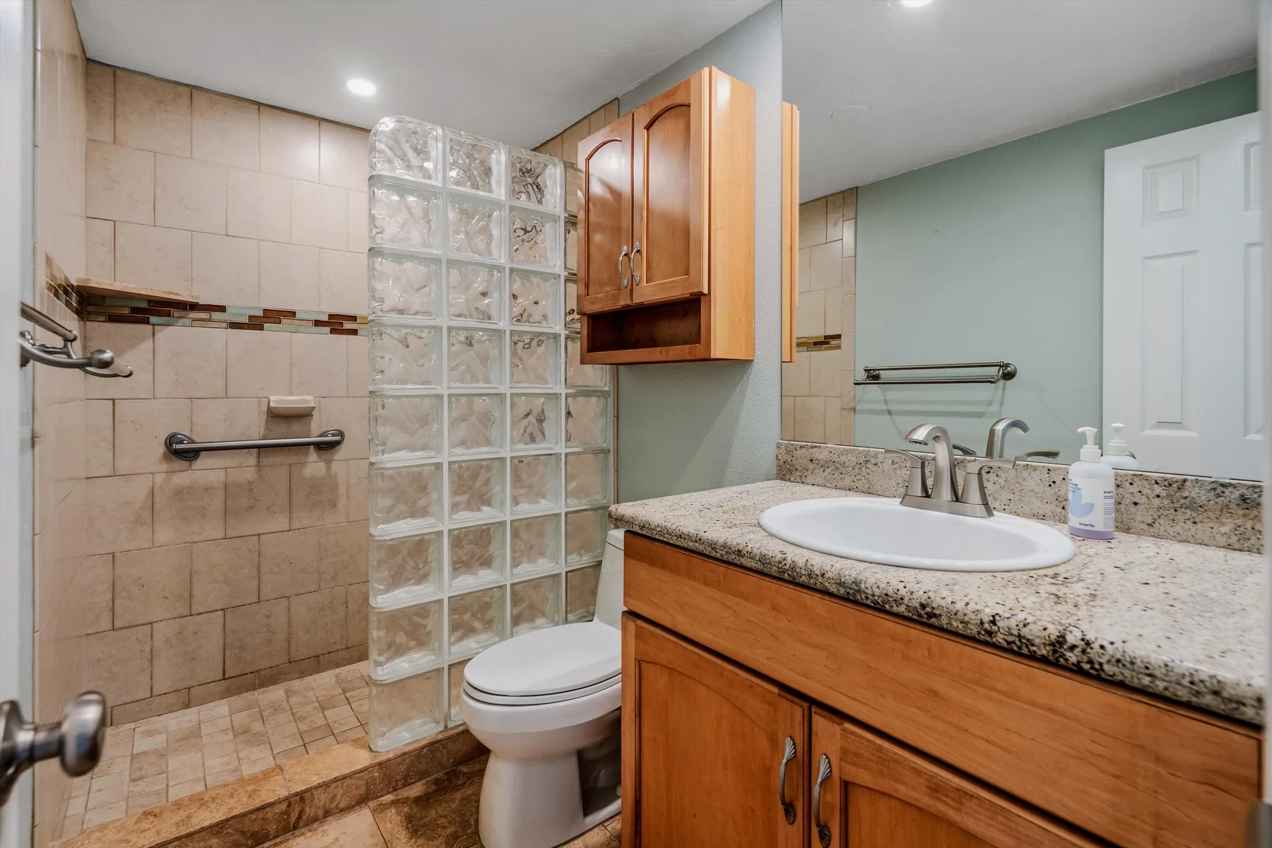 Un baño con azulejos, una división de bloques de vidrio y un tocador con lavabo.