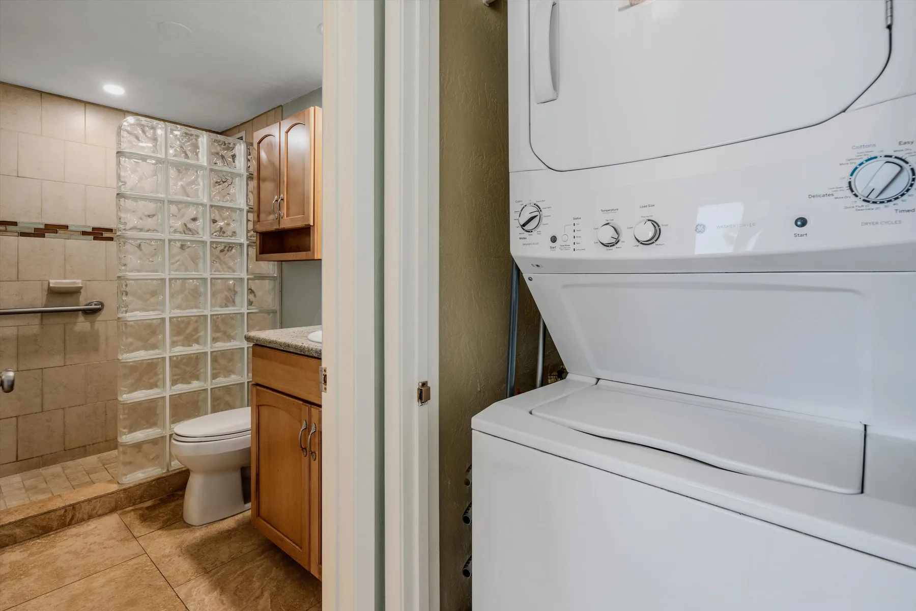 Un baño con inodoro y lavabo está junto a una zona de lavado con lavadora y secadora.
