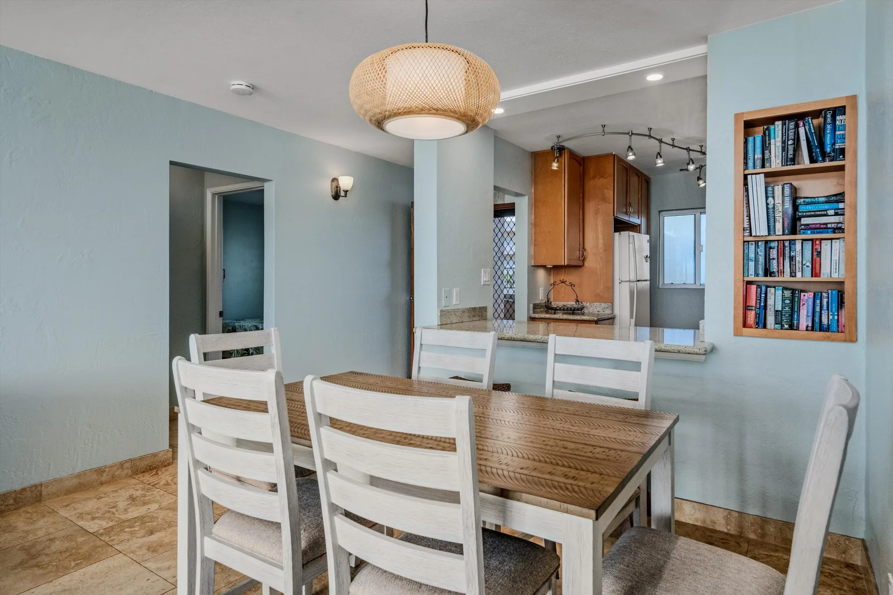Comedor con una mesa de madera y asientos blancos, abierto a una cocina.