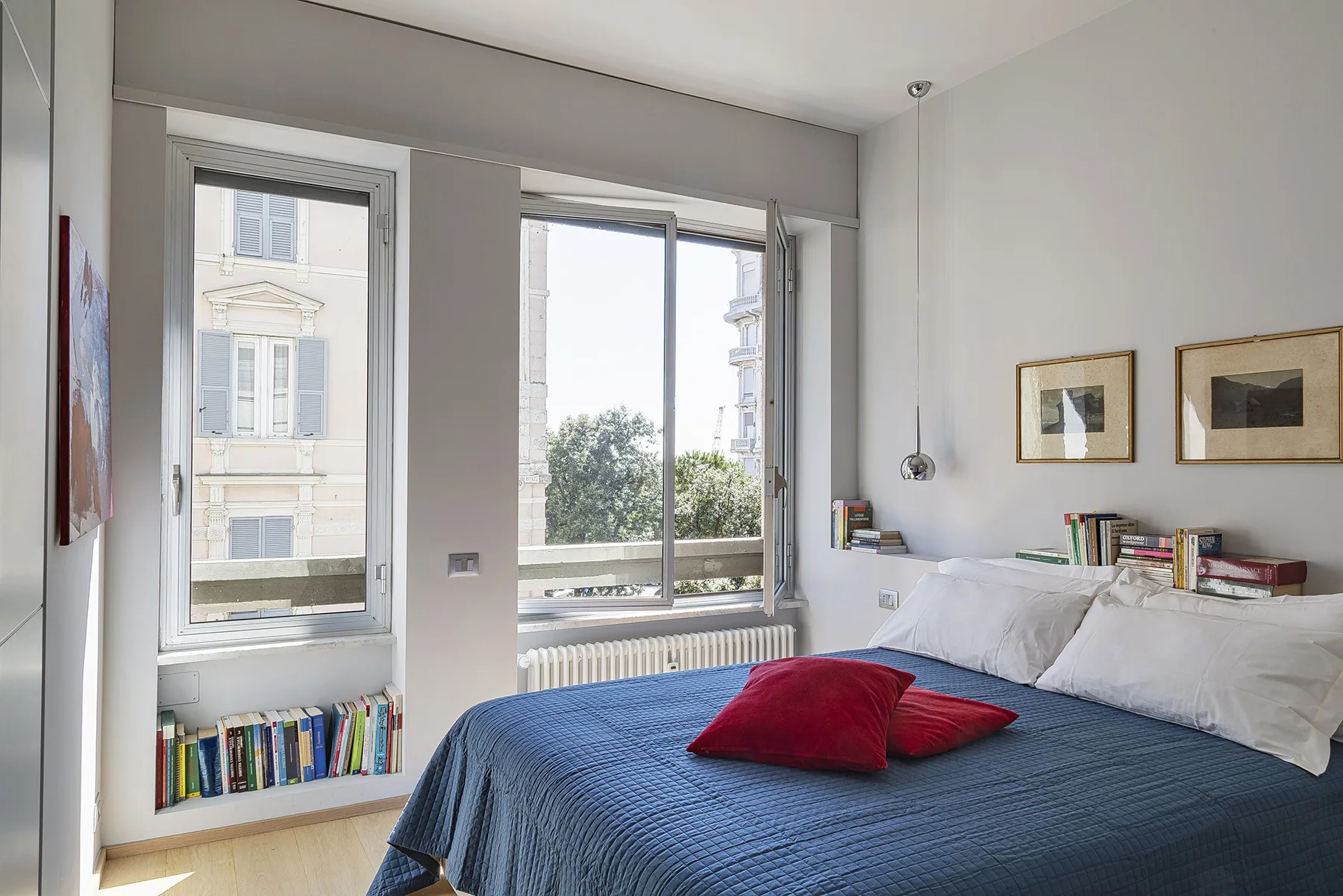 Un dormitorio con una cama cubierta de azul bajo grandes ventanas.