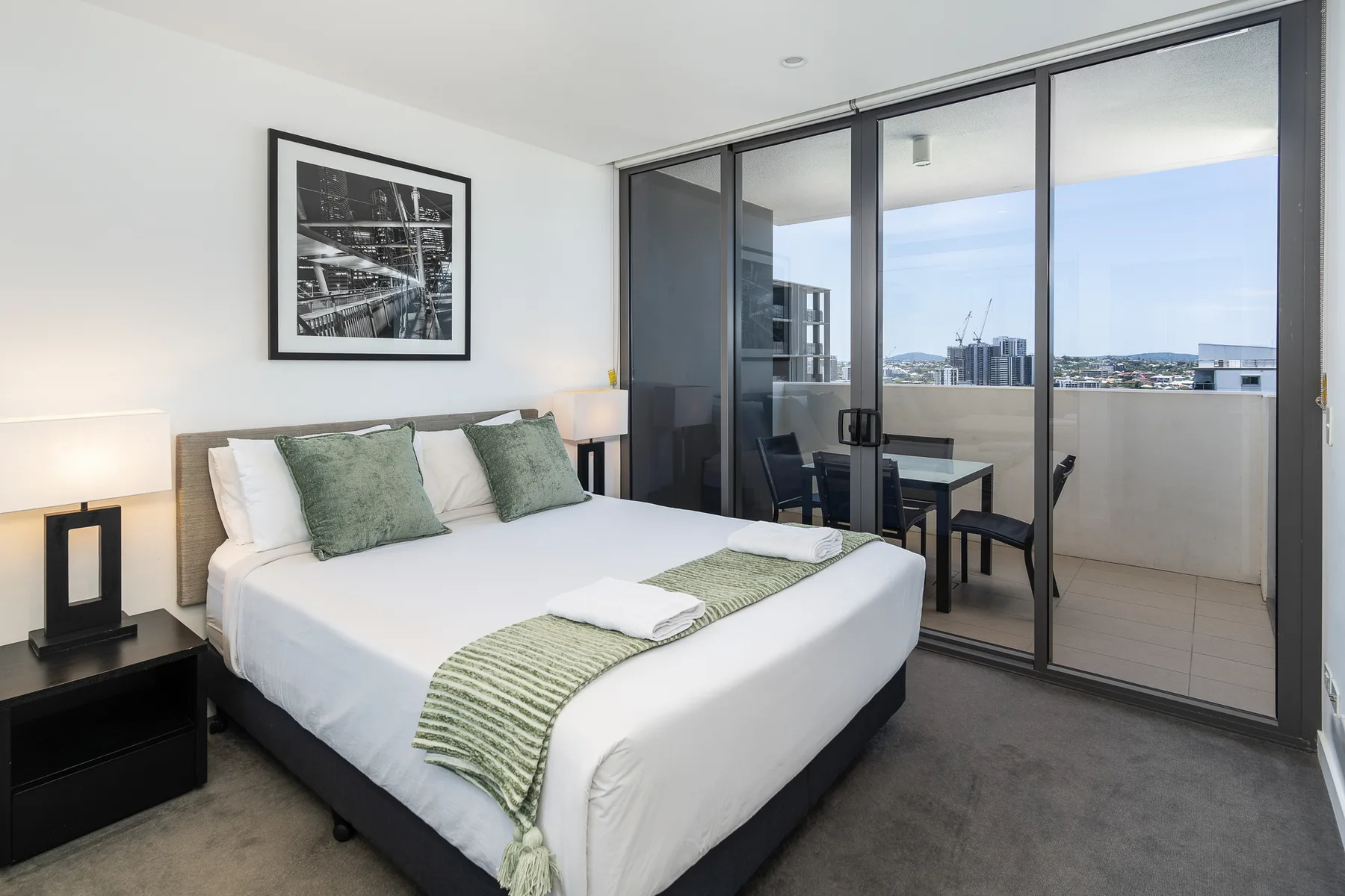 A bedroom with a neatly made bed beside glass doors opening onto a balcony.