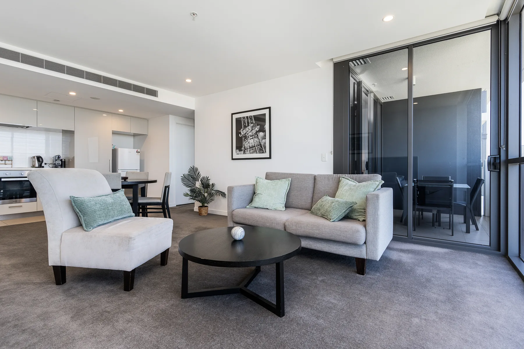 A living room with seating, a coffee table, and a kitchen in the background.