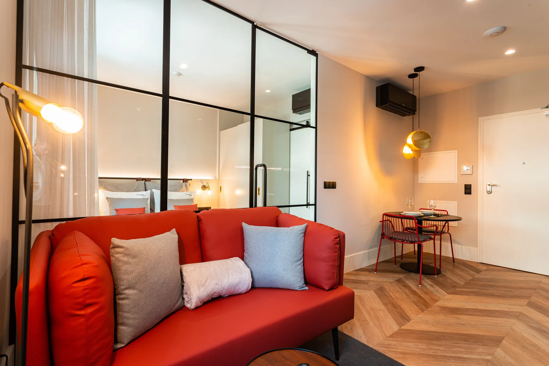 Sala de estar con asientos rojos junto a un dormitorio separado por un tabique de vidrio.