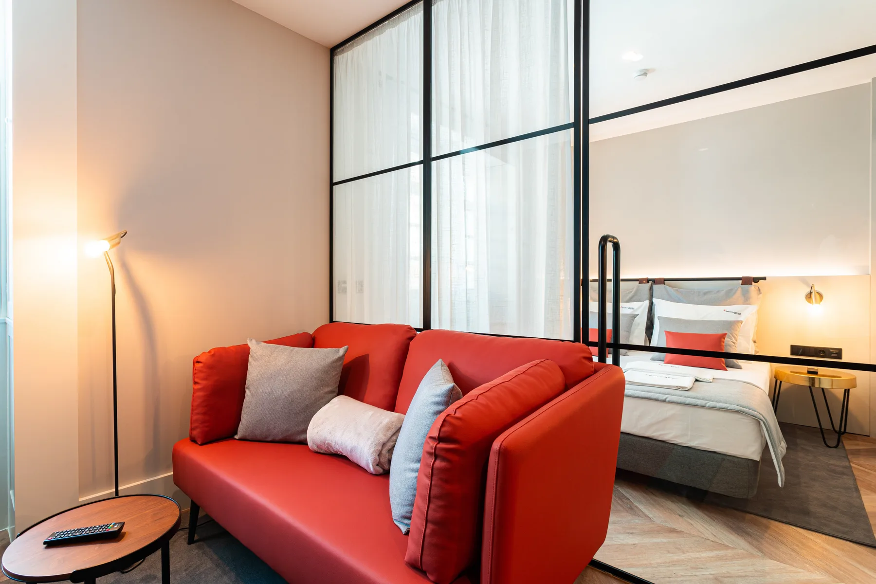Una sala de estar con un sofá rojo junto a un panel de vidrio y un dormitorio.