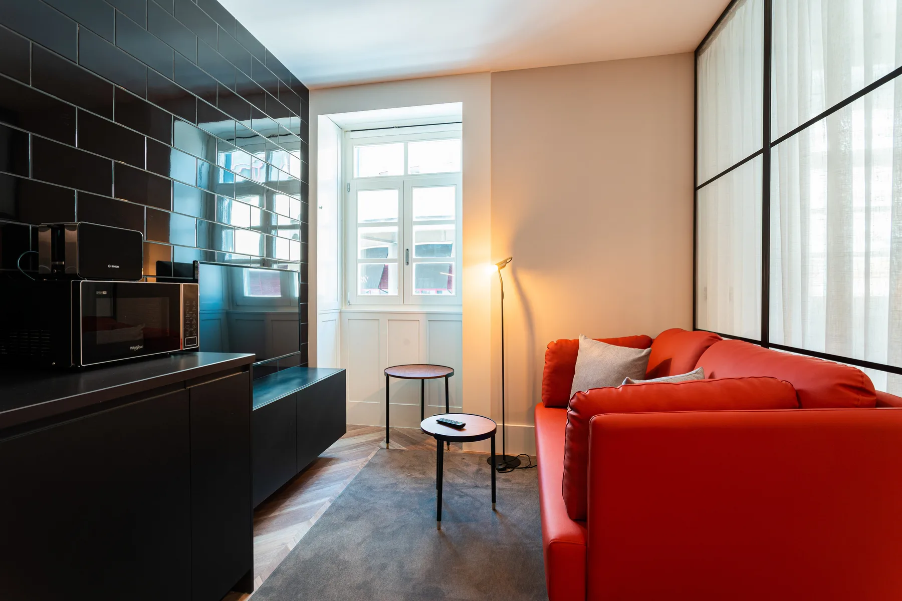 Sala de estar con asientos rojos junto a una cocina compacta negra.