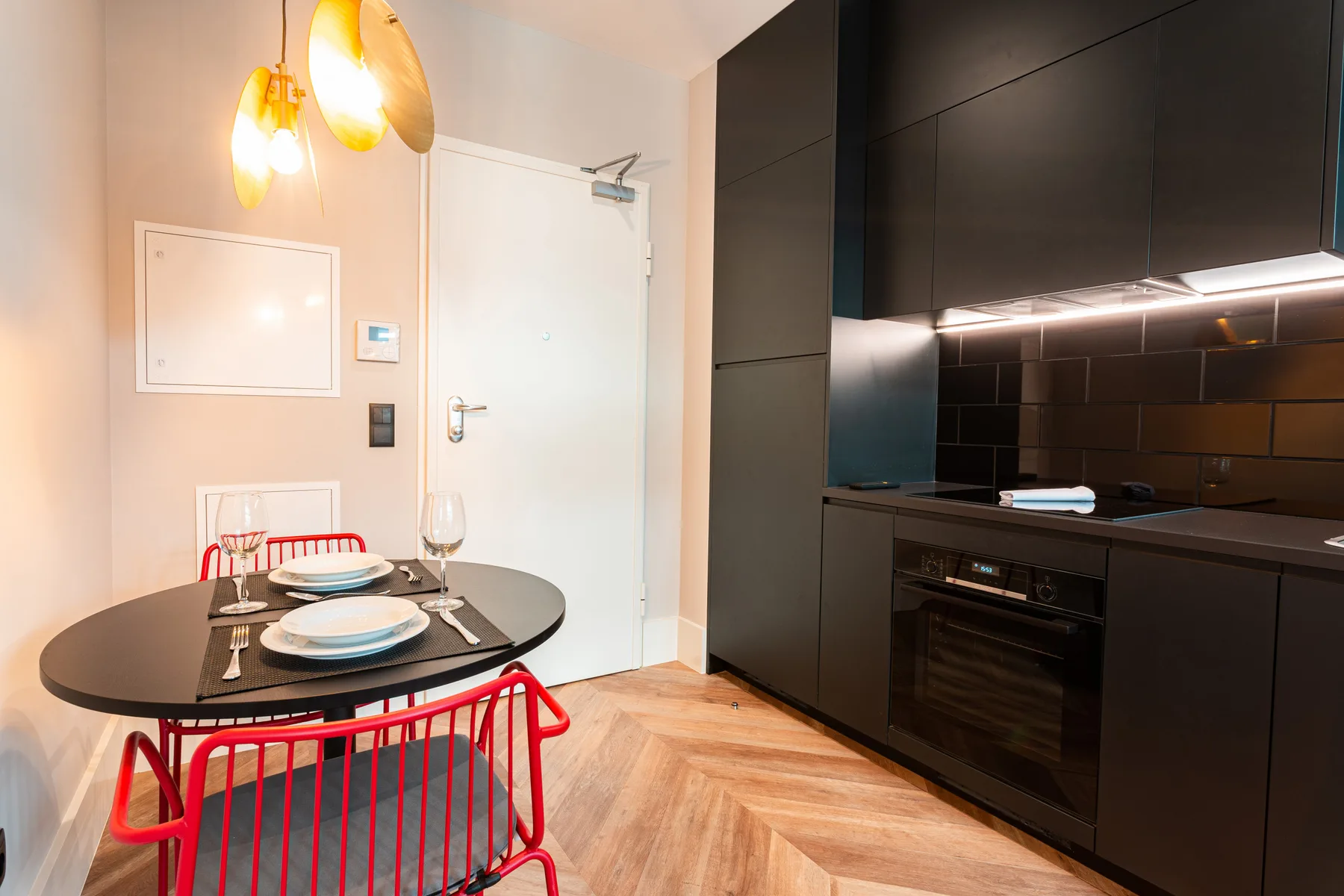 Dining area beside a compact kitchen, with a round table and red seating.