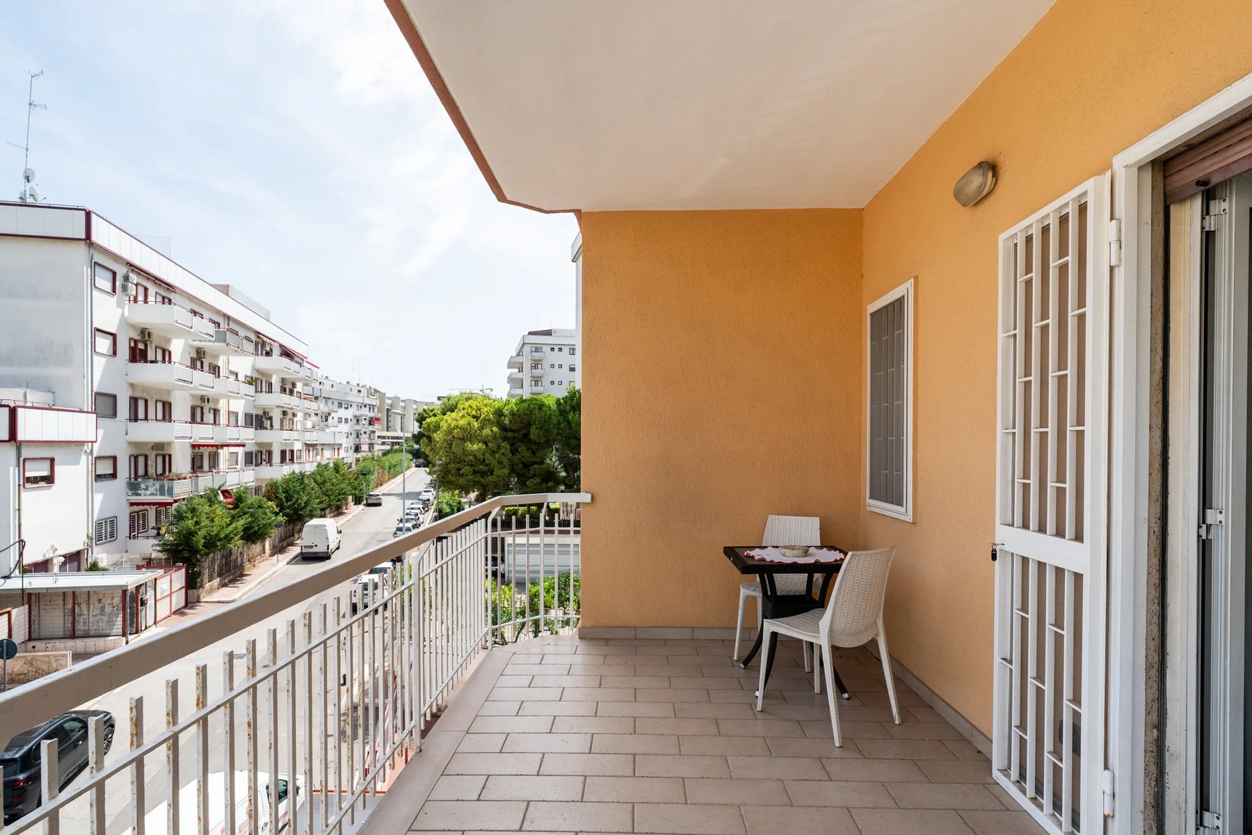 Un balcón cubierto con una mesa pequeña y asientos da a edificios de apartamentos cercanos.