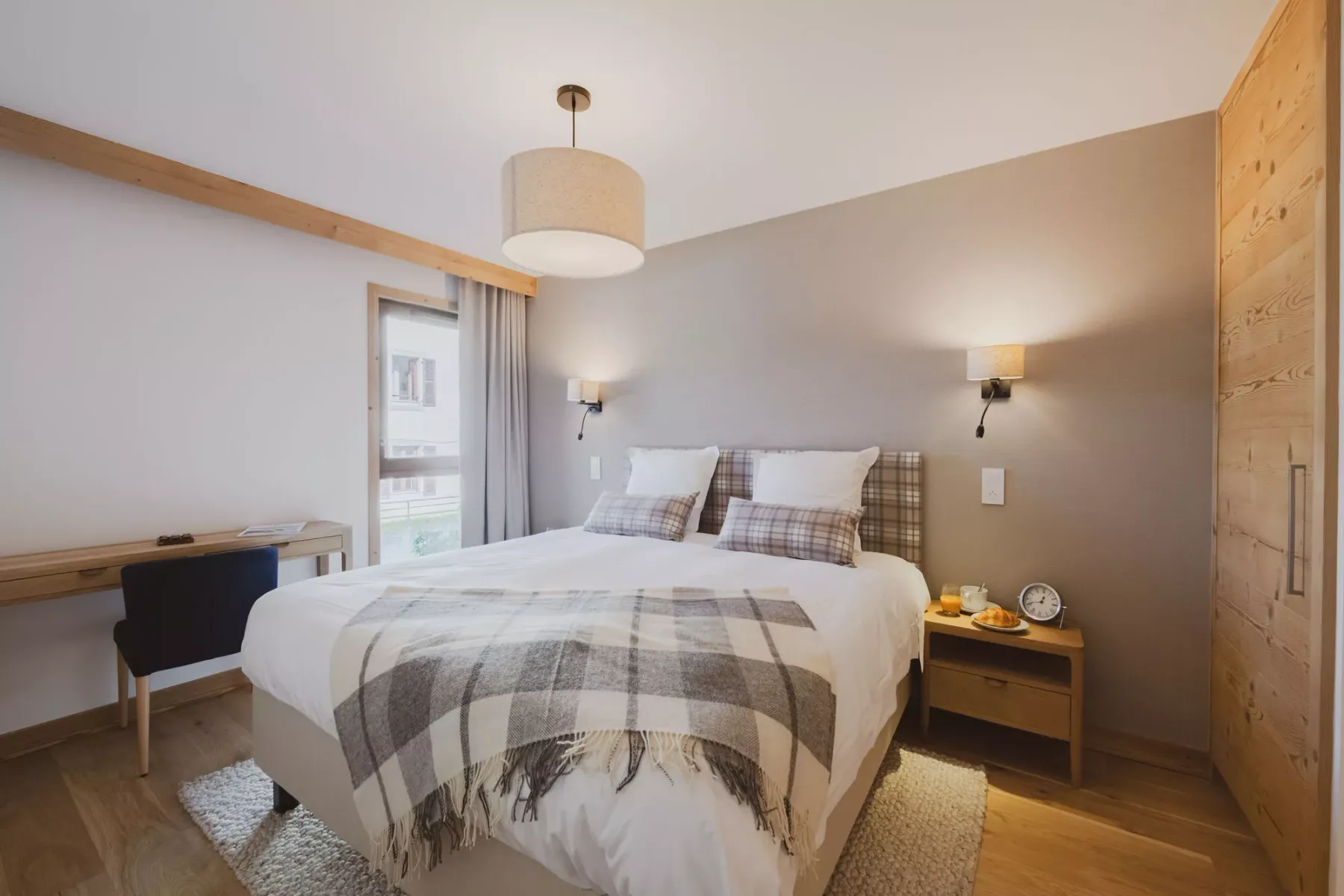 Un dormitorio con una cama doble vestida con ropa de cama blanca y detalles de cuadros.