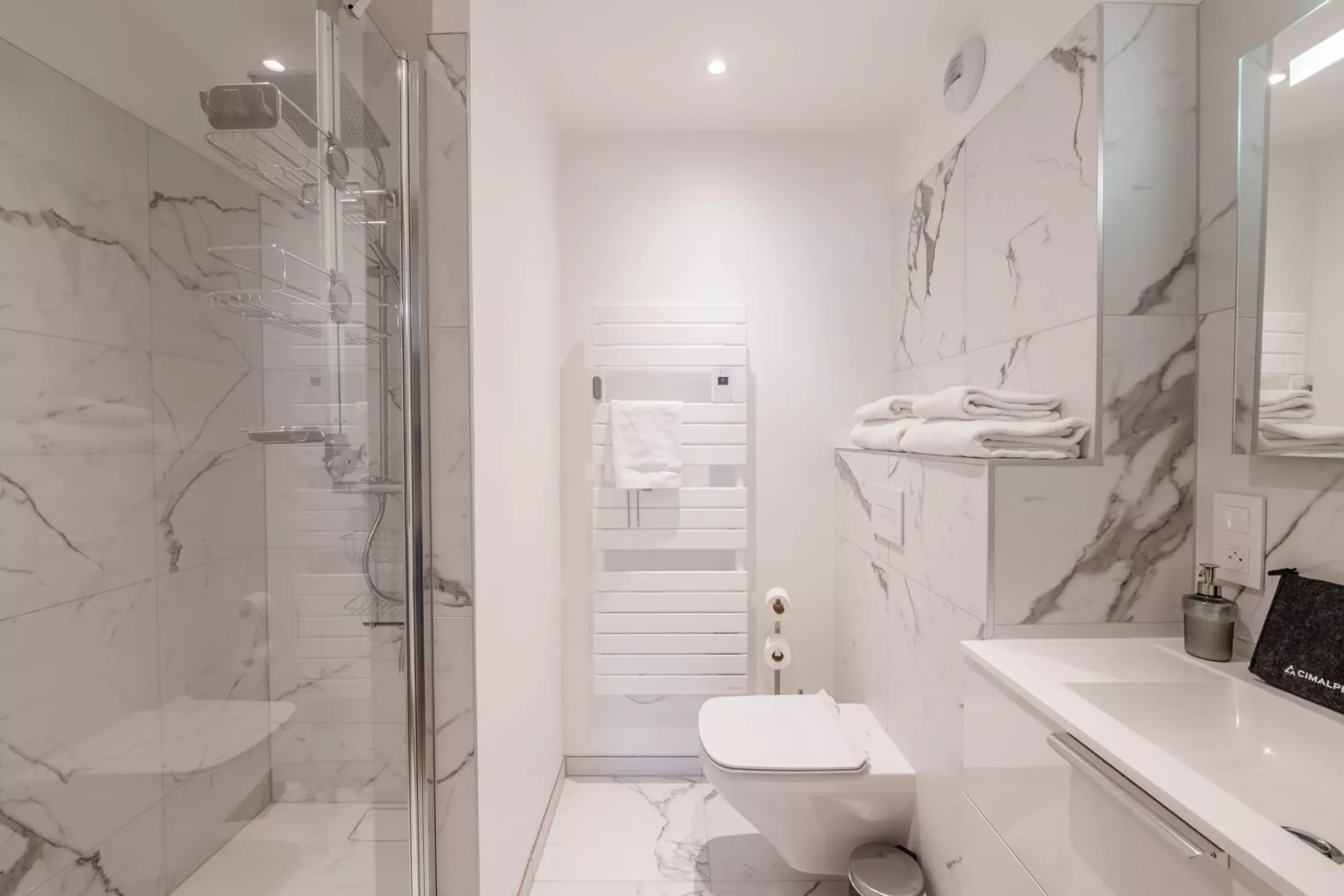 Un baño luminoso de mármol con ducha de vidrio y lavabo blanco.