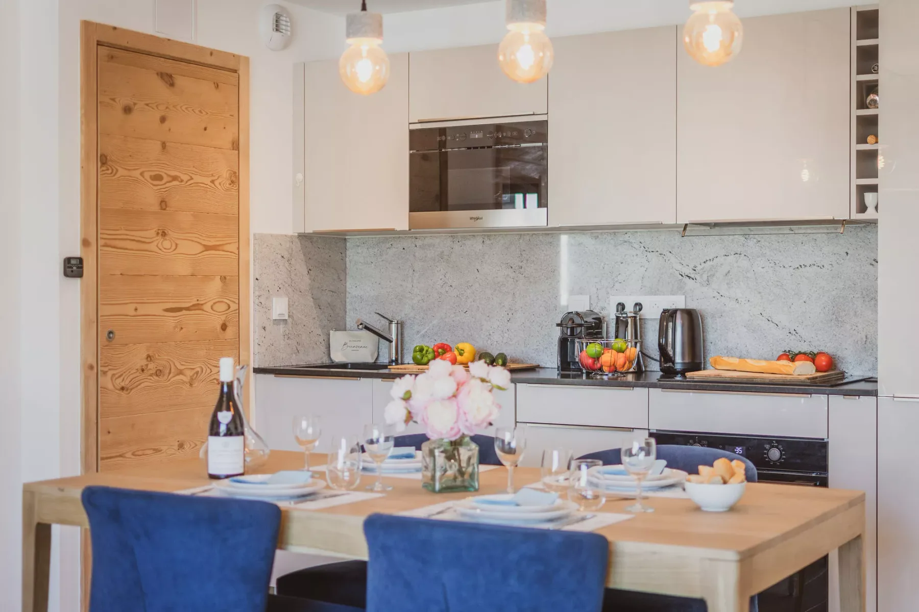 Una mesa de comedor con asientos azules frente a una cocina luminosa.
