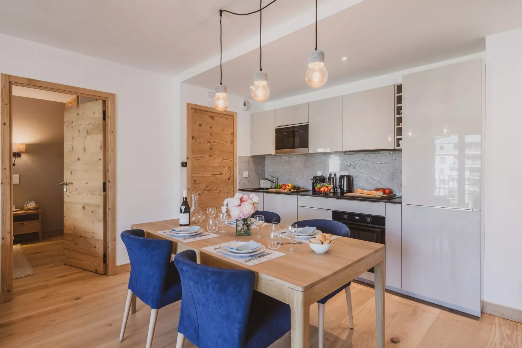 A dining area with a wooden table sits beside a modern kitchen.