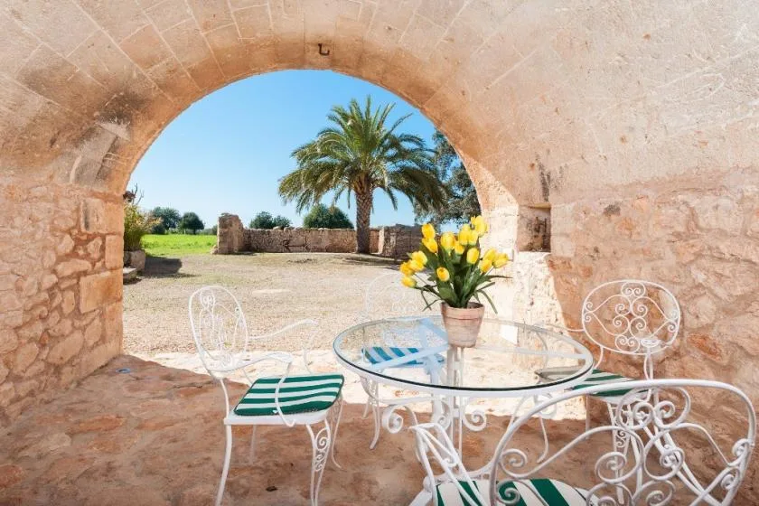 Una zona de estar en un patio bajo un arco de piedra da a un jardín con palmeras.