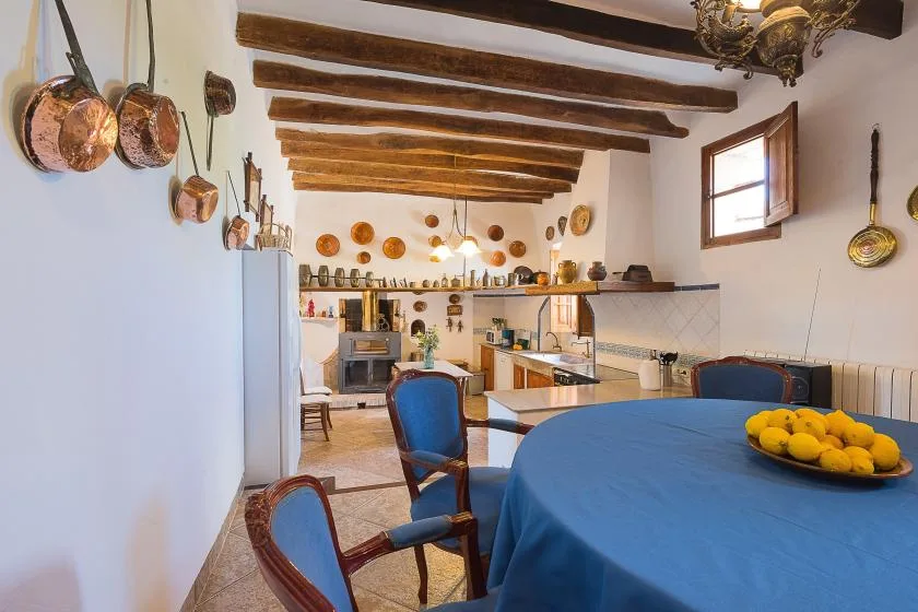 Una cocina rústica con comedor, mesa cubierta de azul y vigas de madera a la vista.