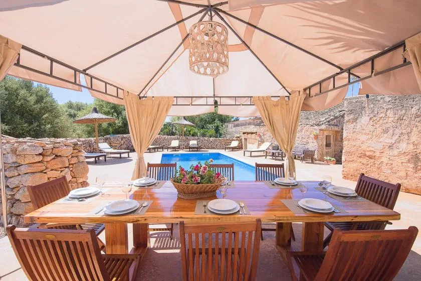 Un comedor exterior cubierto da a una piscina y un patio de piedra.