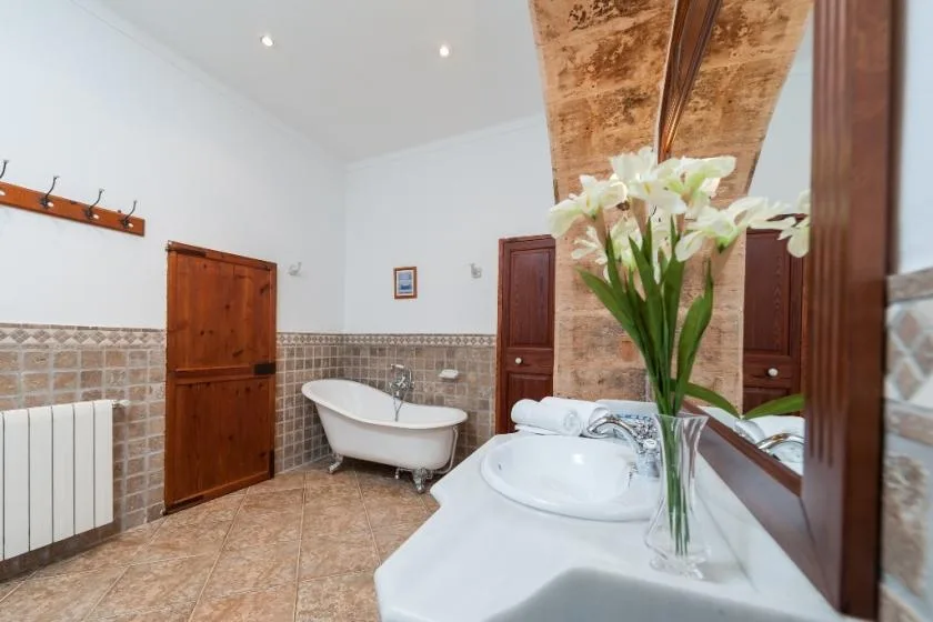 Un baño con azulejos, bañera, lavabo y flores blancas.