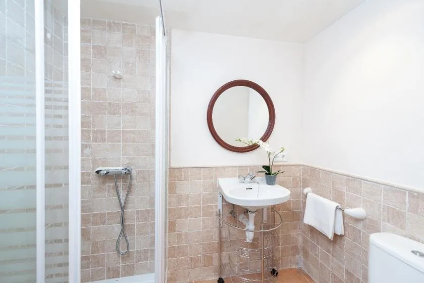 Un baño con azulejos, ducha de vidrio, lavabo suspendido y espejo redondo.
