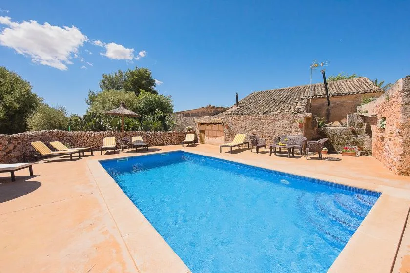 An outdoor swimming pool sits beside a stone patio with seating.