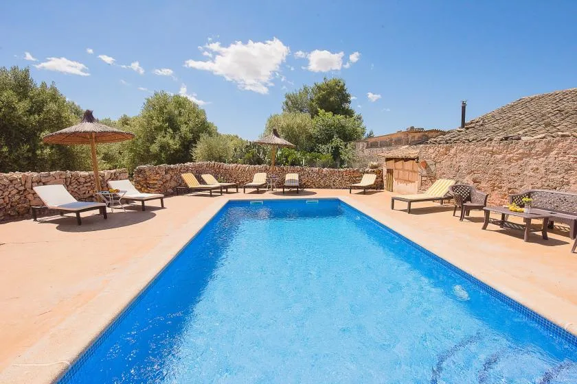 An outdoor swimming pool is surrounded by lounge seating and stone walls.
