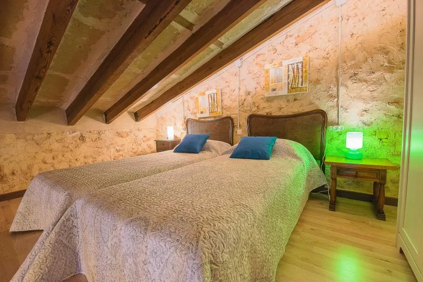 Un dormitorio con dos camas bajo un techo inclinado y vigas de madera a la vista.