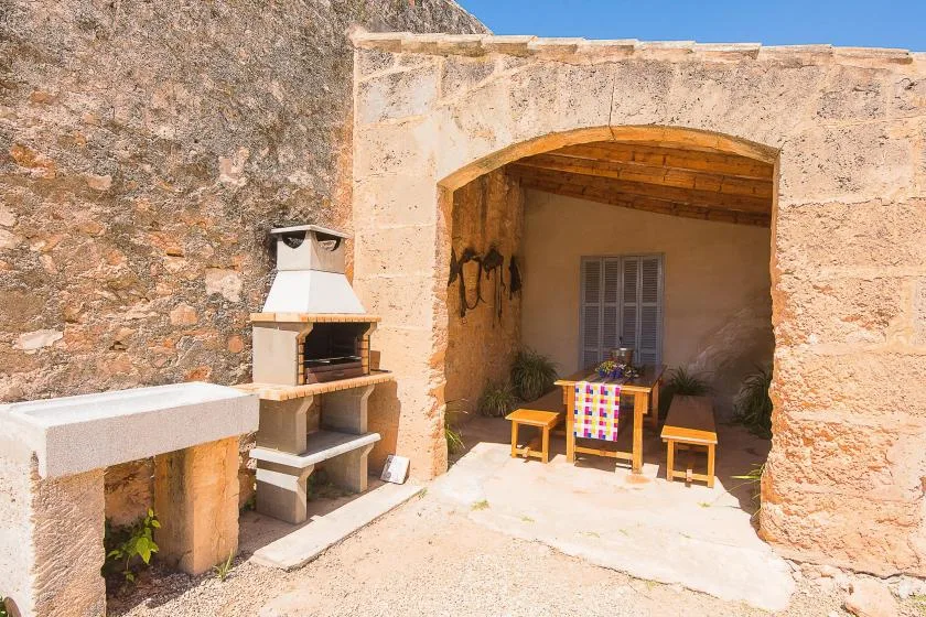 Zona de comedor exterior de piedra bajo un arco, con una mesa y bancos.