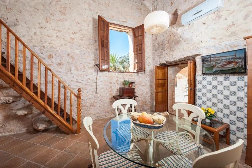 Comedor con mesa de vidrio y una escalera de madera junto a una ventana abierta.