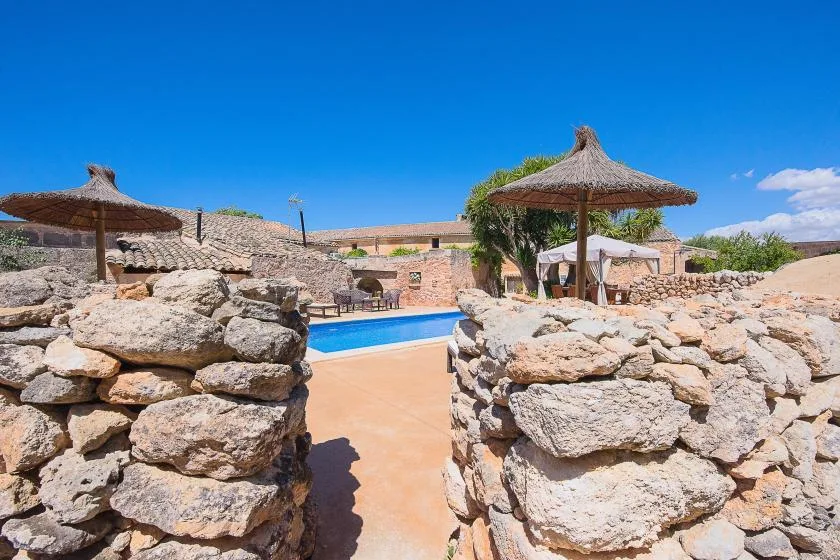 Una piscina al aire libre está enmarcada por muros de piedra y sombrillas de paja.