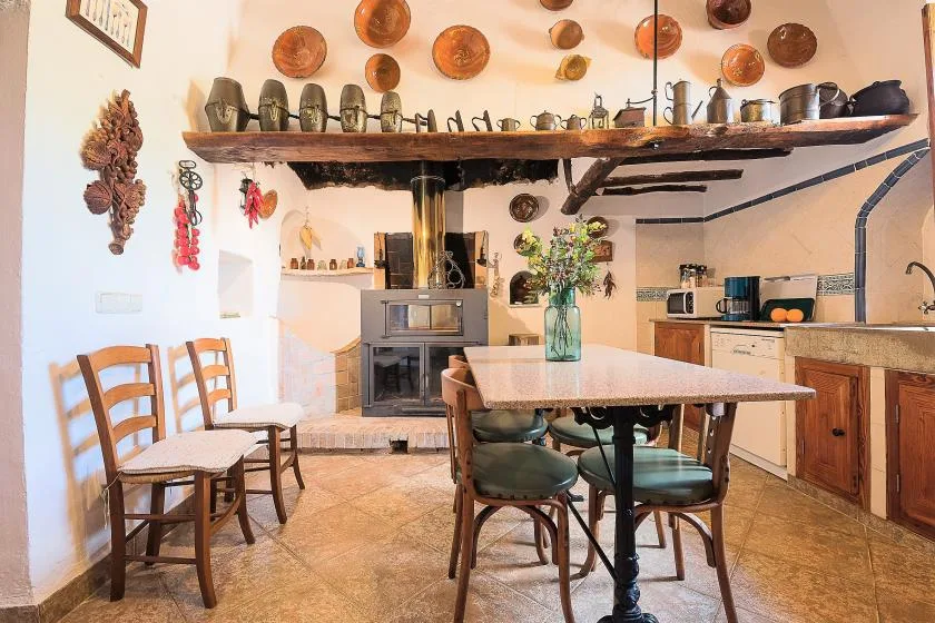 Una cocina y comedor rústicos con una mesa larga bajo utensilios colgados.
