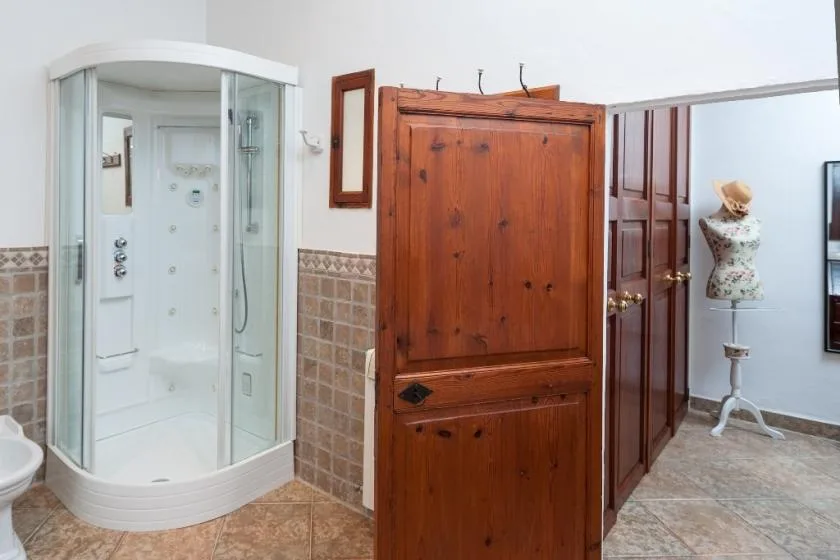 Un baño con una ducha de vidrio junto a un armario grande de madera.