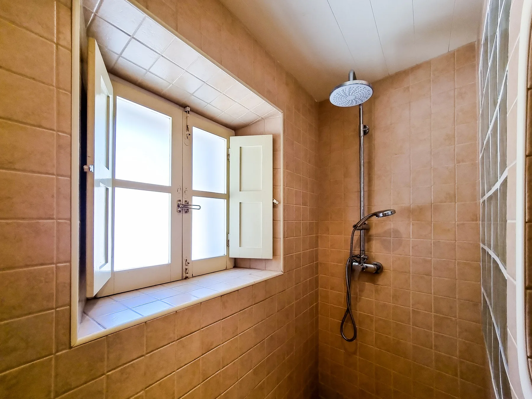 A tiled bathroom with a shower beside a large window.