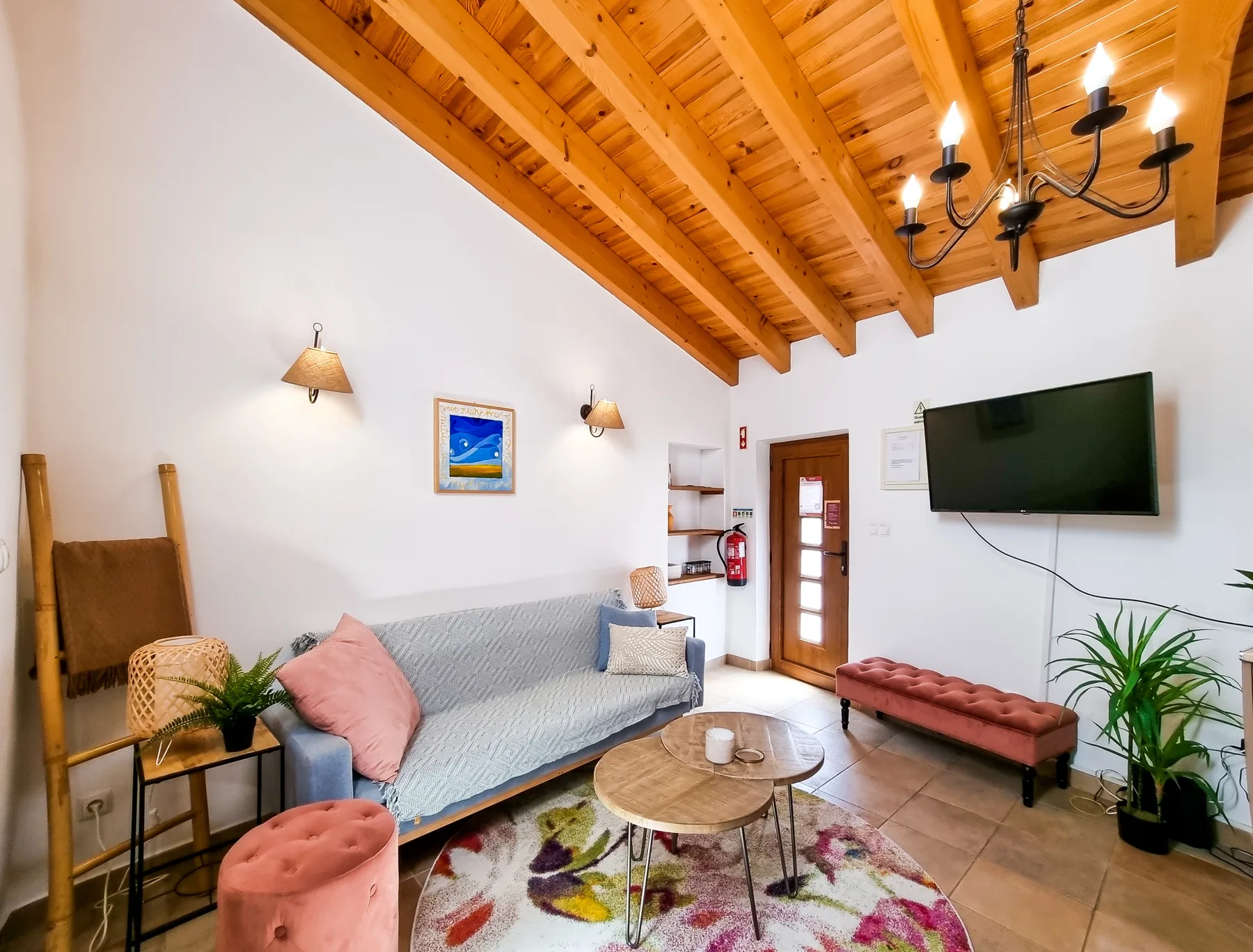 A living room with a gray sofa, wooden ceiling beams, and a wall-mounted television.