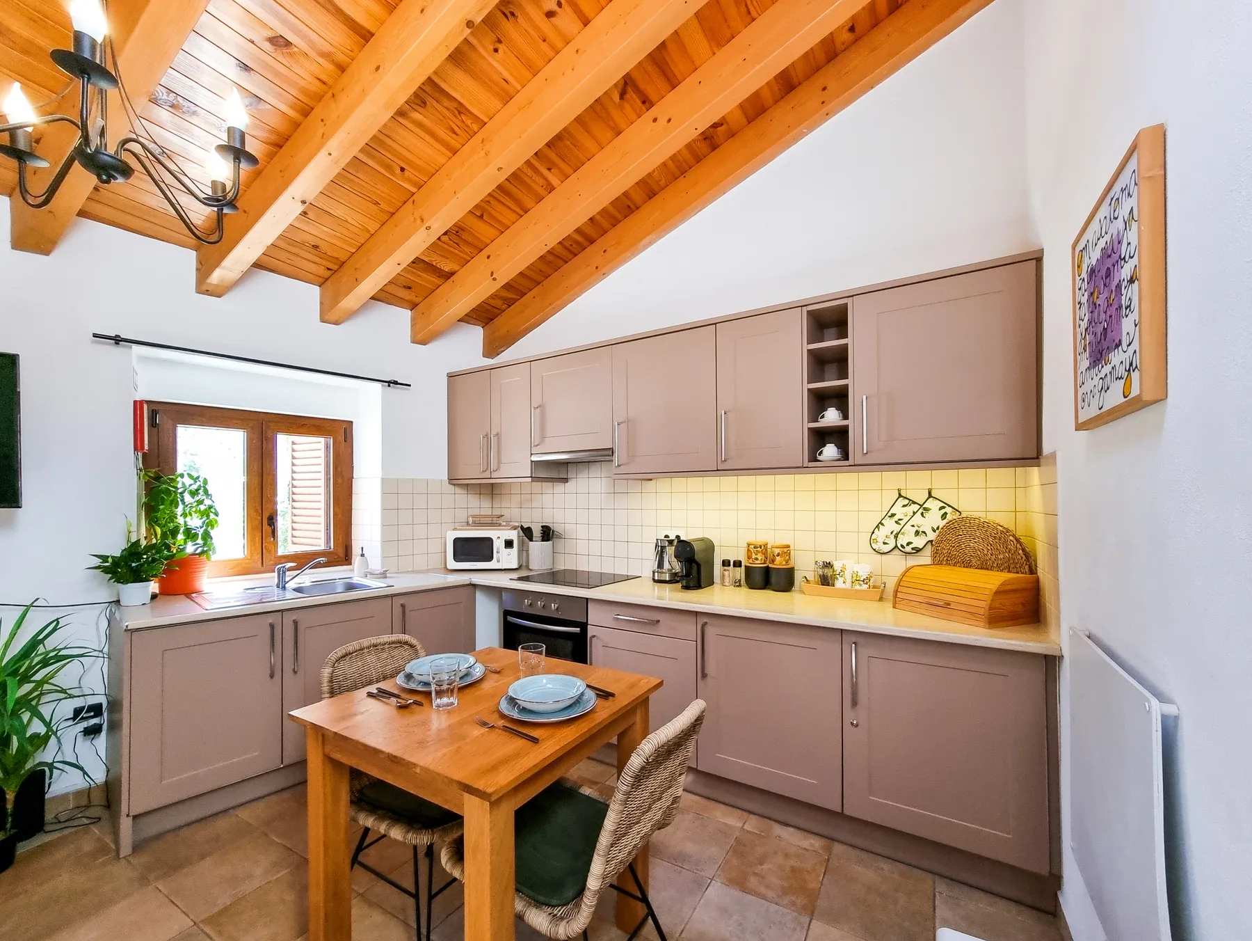 A kitchen with a wooden dining table beneath a sloped timber ceiling.