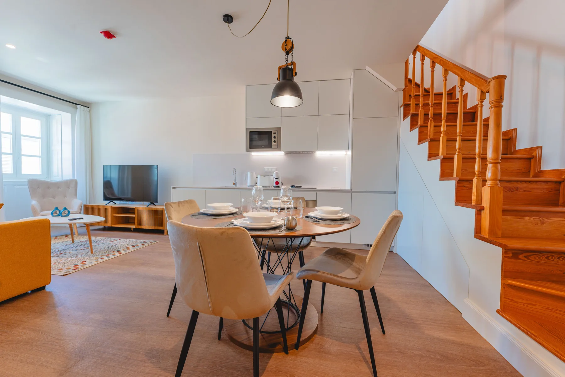 Sala de estar y comedor de planta abierta, con cocina y una escalera de madera.