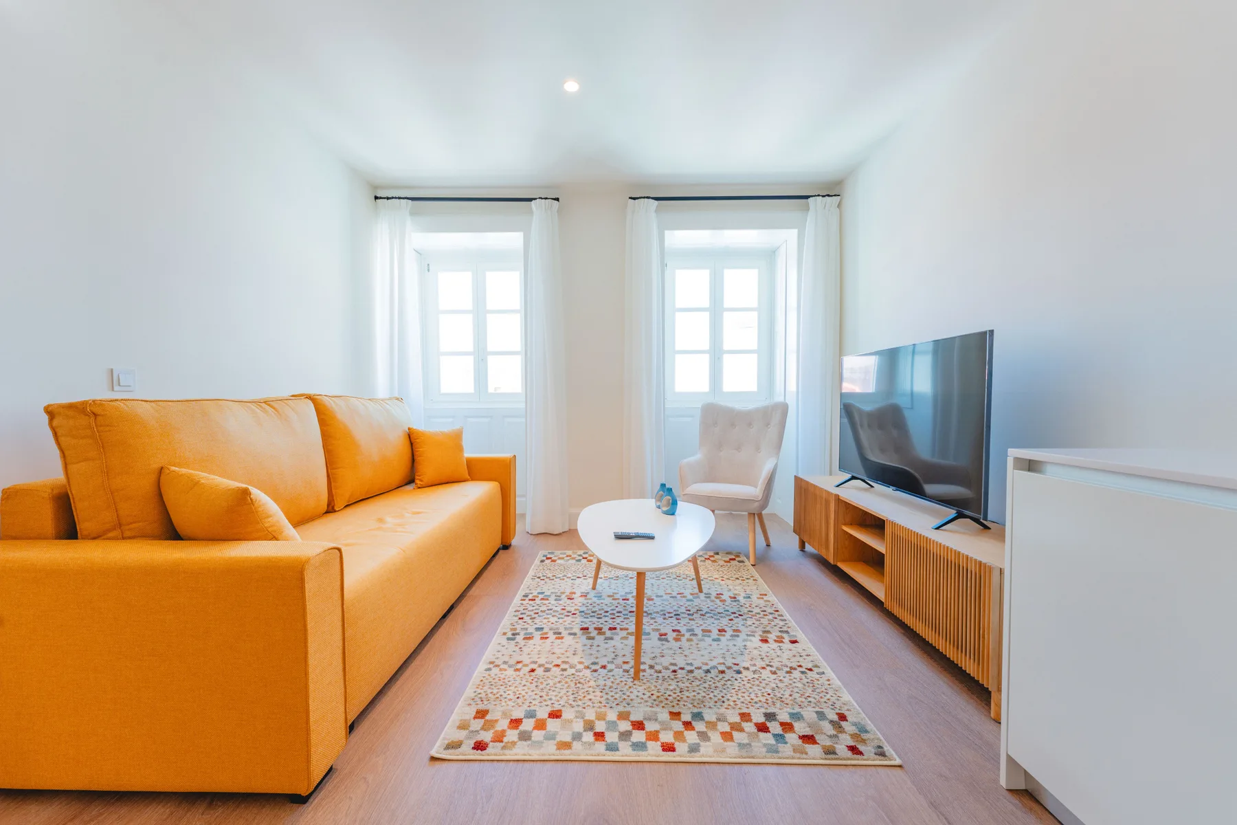 Una sala luminosa con asientos naranjas, un televisor y una alfombra estampada.