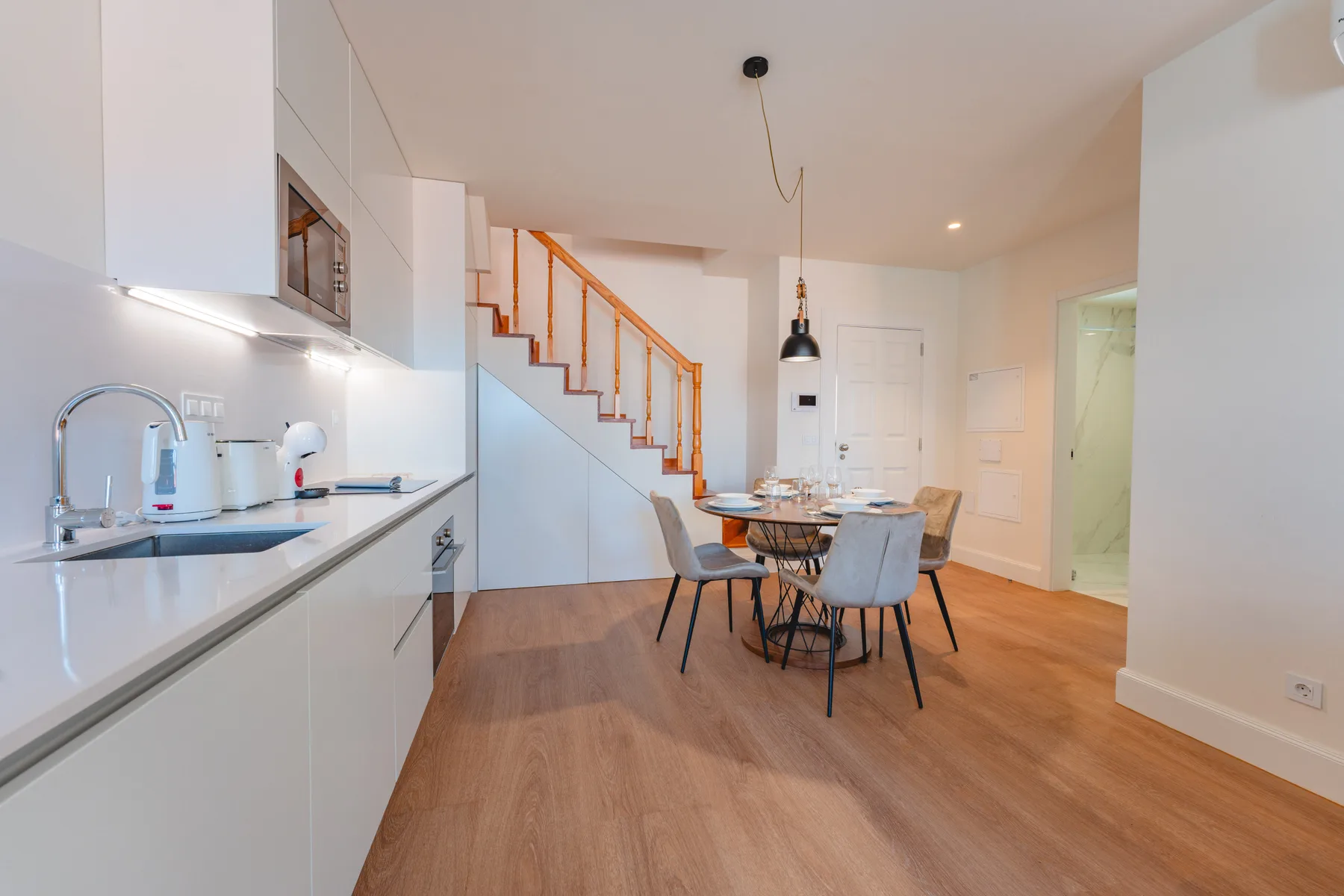 Una cocina y comedor de concepto abierto con una escalera y suelo de madera.