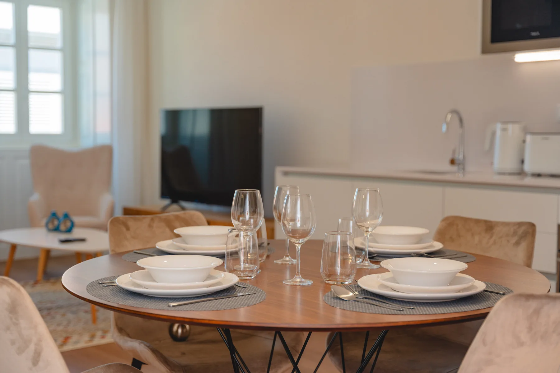 Una mesa de comedor está puesta con platos y vasos en un comedor luminoso.