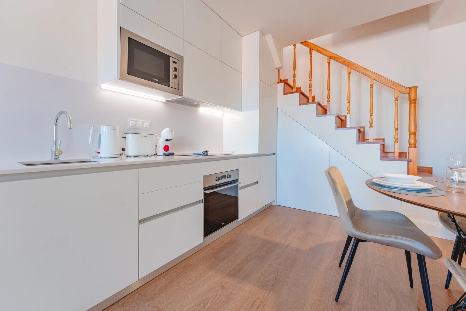 Una cocina y comedor luminosos con una escalera junto a la mesa.