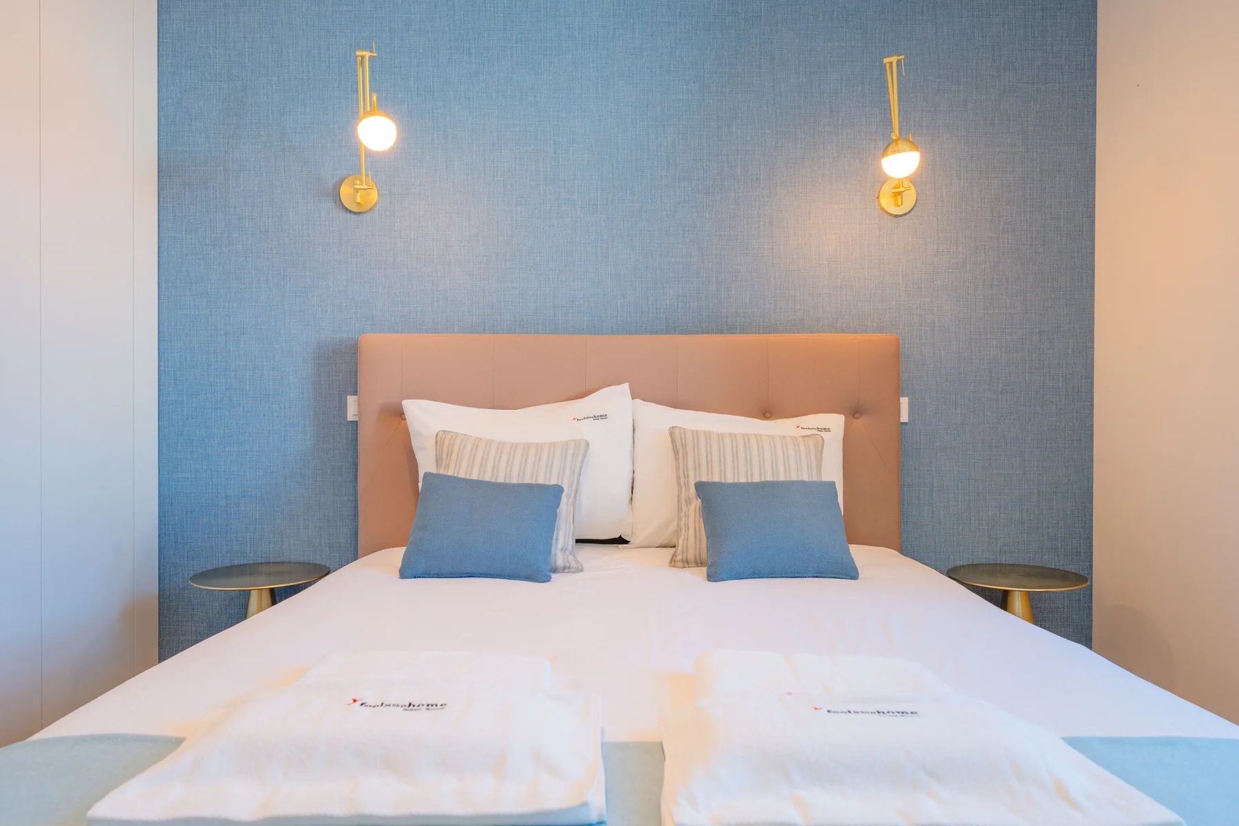 Un dormitorio con una cama bien tendida, una pared azul y mesitas de noche.